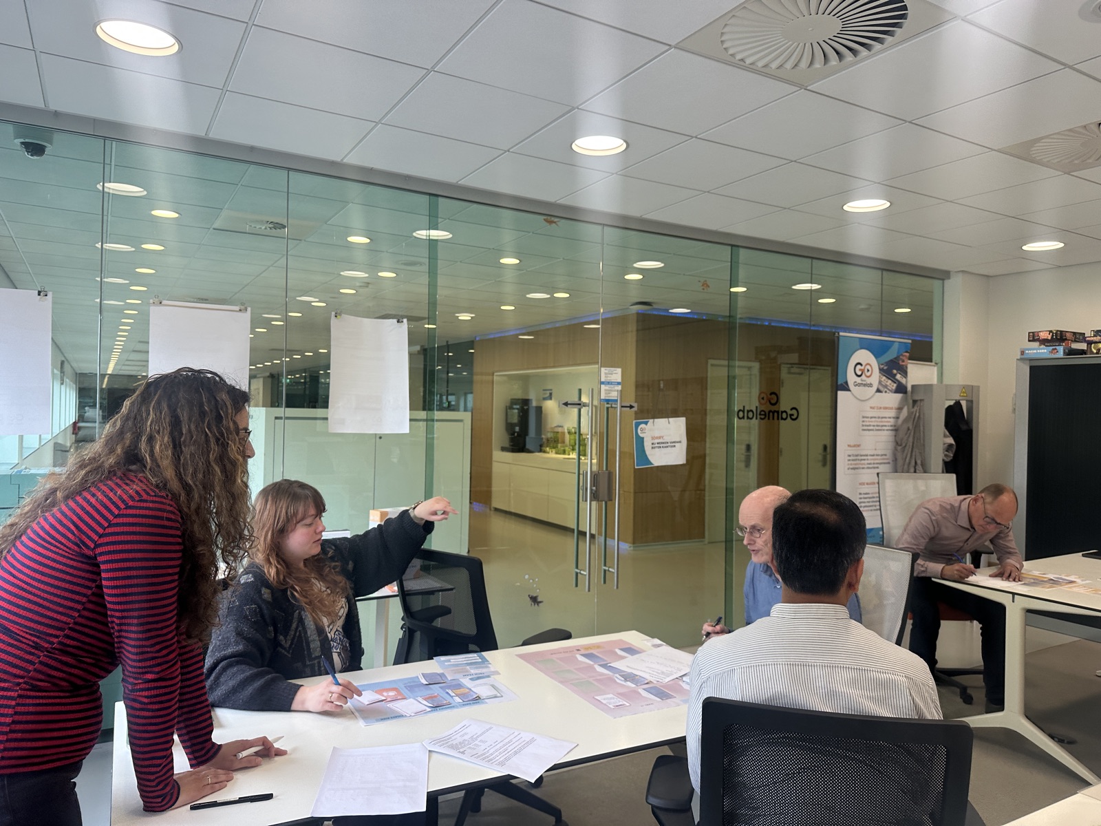 Five people around a table at the TU Delft Gamelab, working through an early version of the game with boards and cards laid out in front of them.